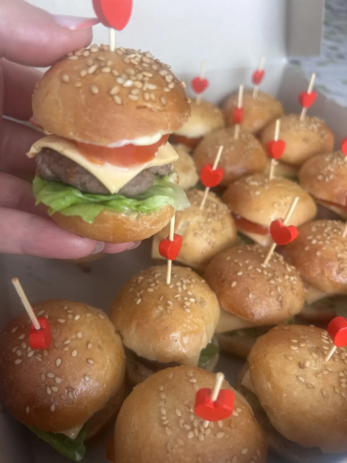 Mini-burger fait maison tenu à la main, piqué d'un cœur rouge